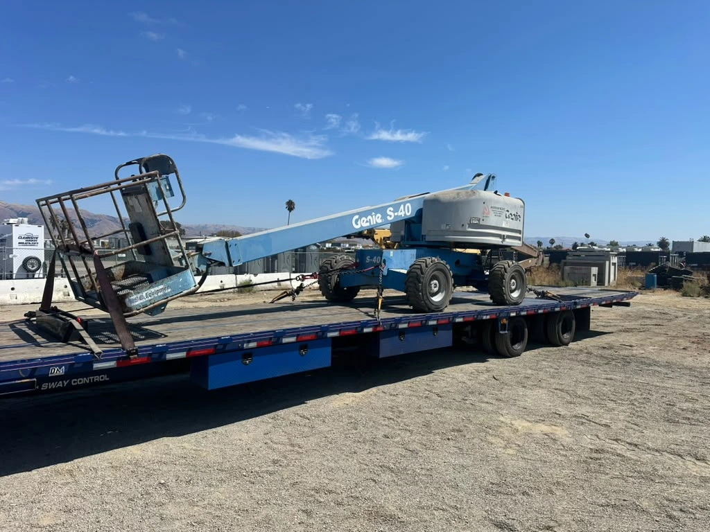 Blue Genie S-40 telescopic boom lift secured on a flatbed trailer for heavy equipment transport