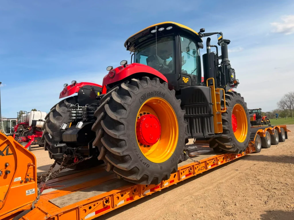 Red and yellow farm tractor chained to an orange lowboy trailer for heavy equipment transport