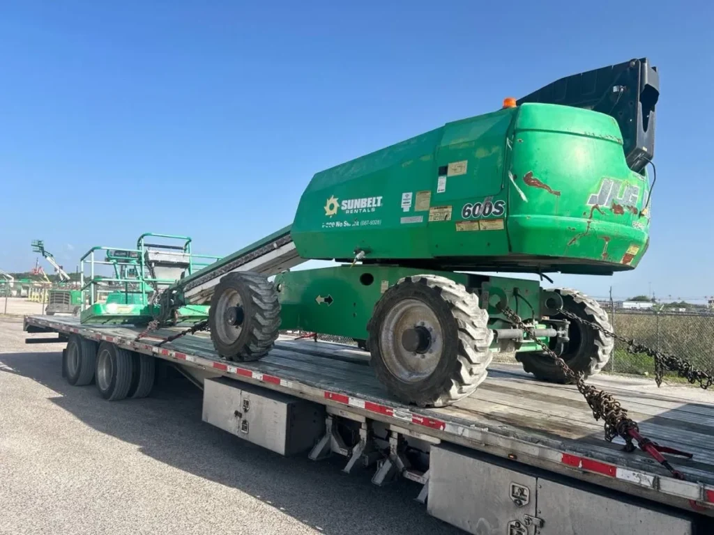 Green JLG telescopic boom lift chained to a flatbed trailer for heavy equipment transport